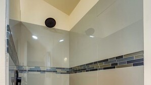 Een douche met een glazen deur, betegelde vloer en een plafondlamp.