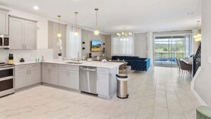 Une cuisine moderne dotée d’un îlot central, d’appareils électroménagers en acier inoxydable et de luminaires suspendus.