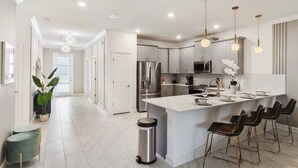 Une cuisine moderne dotée d’un îlot central, d’appareils électroménagers en acier inoxydable et de luminaires suspendus.