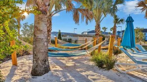 Une zone de plage avec des hamacs, des palmiers et un parasol bleu.