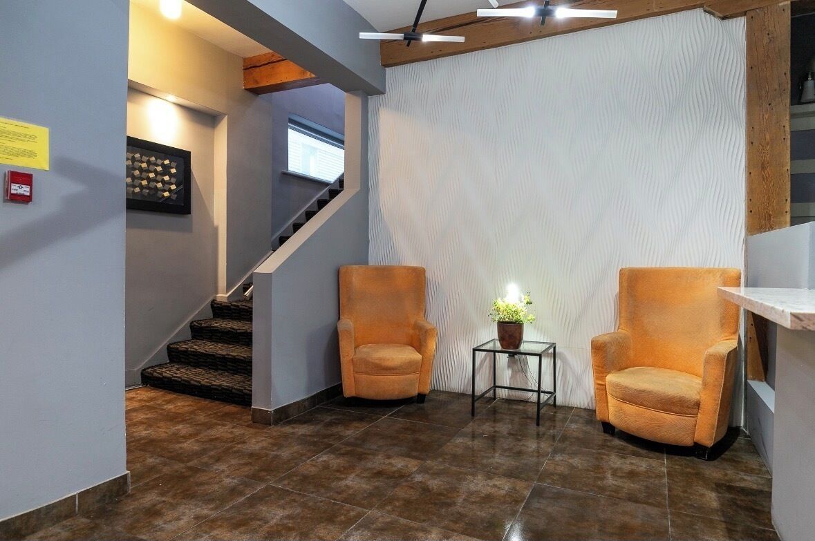 Un hall con una escalera, dos sillones, una pequeña mesa con una planta y una lámpara en la pared.