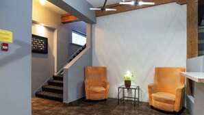 Een hal met een trap, twee fauteuils, een kleine tafel met een plant en een wandlamp.