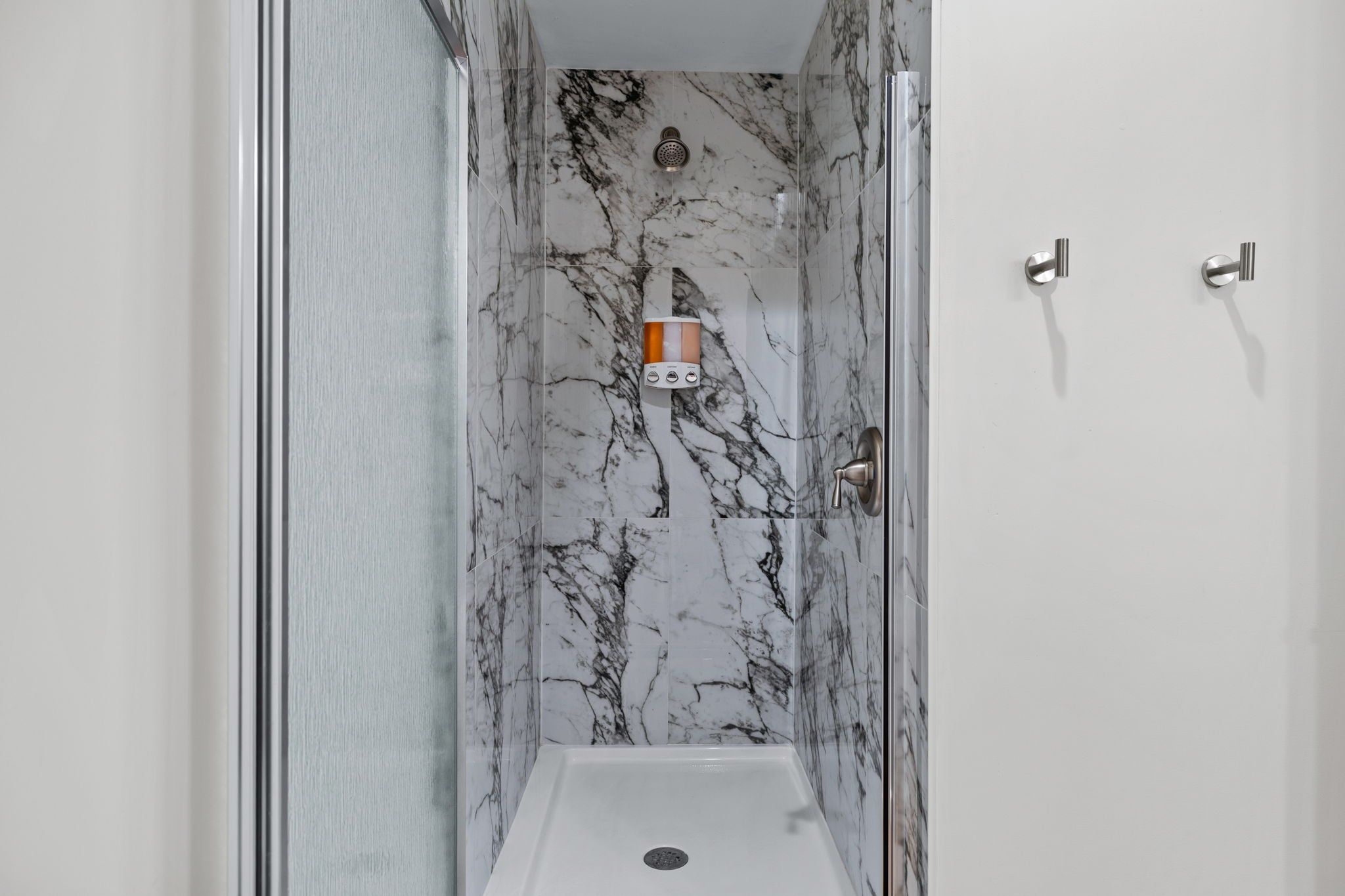 A bathroom with a shower stall, marble walls, and a towel dispenser.