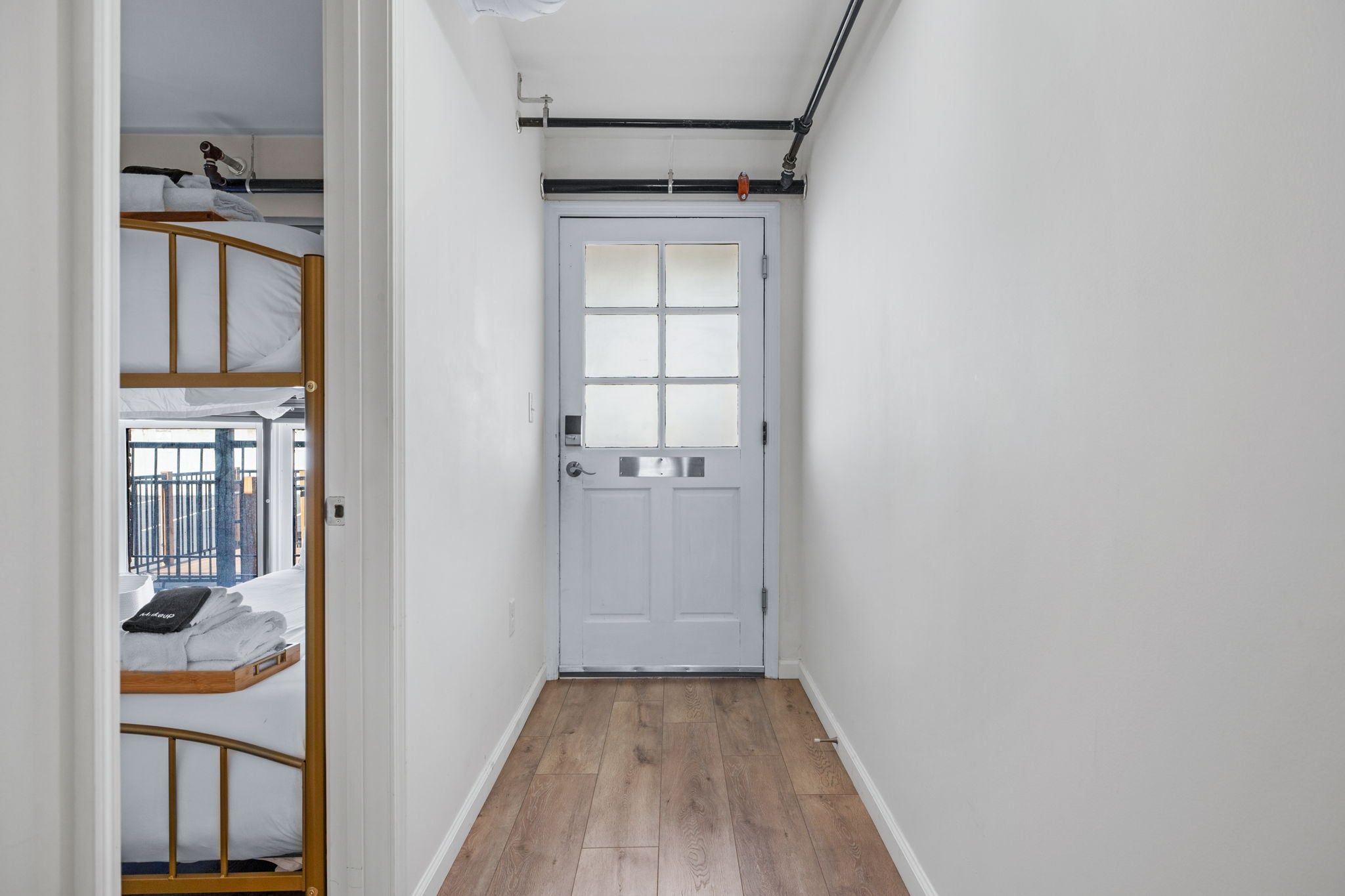 A narrow hallway with a wooden floor leading to a white door with a window.