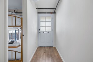 A narrow hallway with a wooden floor leading to a white door with a window.