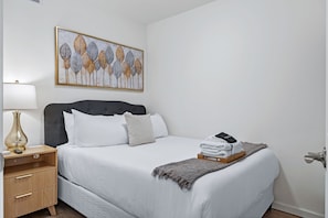 A neatly arranged bedroom with a bed, bedside table, lamp, and a wall-mounted artwork. - Elegant 2BR | St Charles Entertainment Area (Saint Charles)