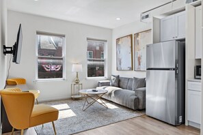 A modern living room with a sofa, a yellow chair, a coffee table, and a large refrigerator. - Elegant 2BR | St Charles Entertainment Area (Saint Charles)