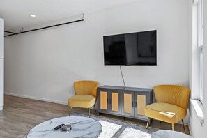 A modern living room with a flat-screen TV mounted on the wall, two yellow armchairs, a grey cabinet with woven doors, and a marble coffee table. - Elegant 2BR | St Charles Entertainment Area (Saint Charles)