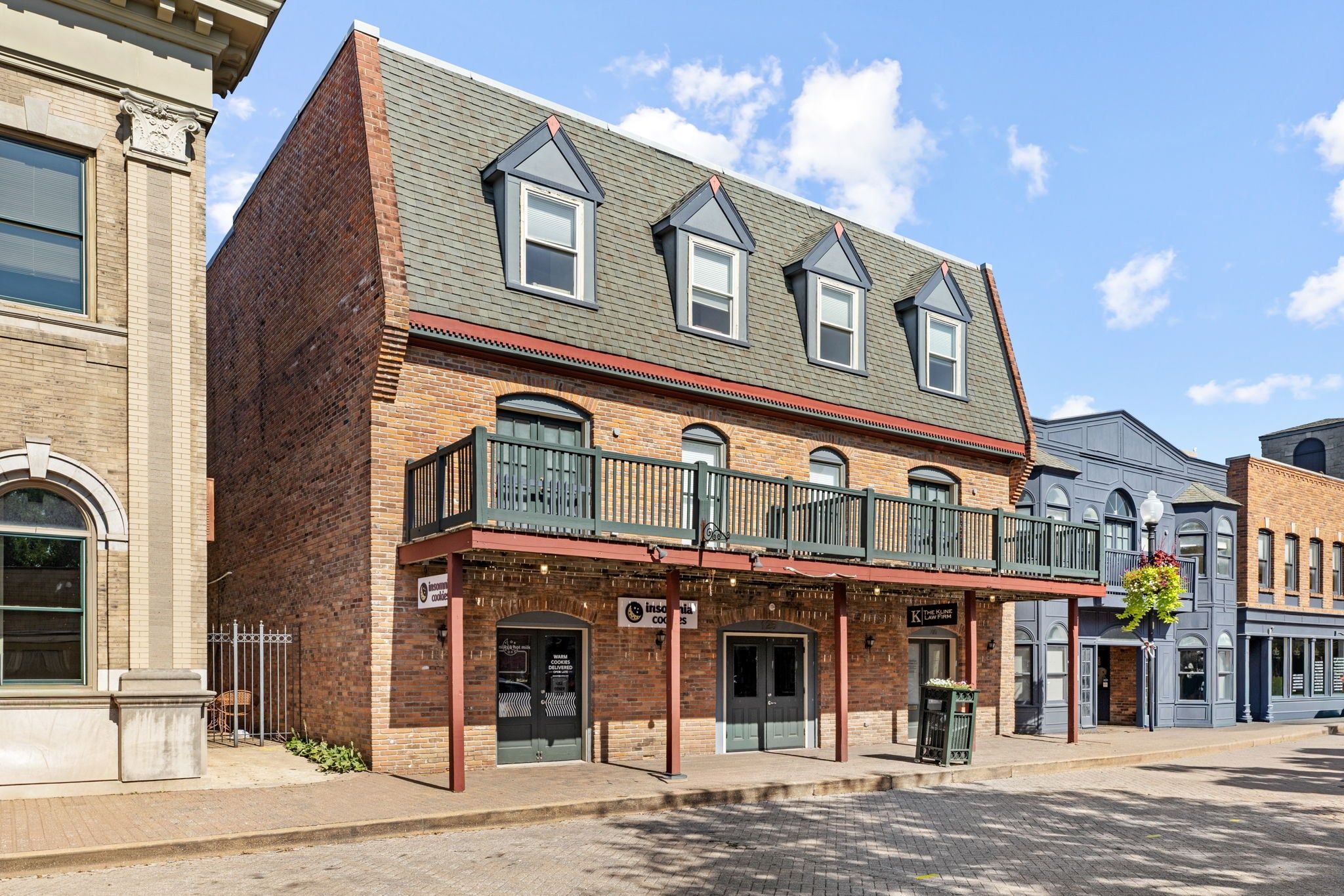 A two-story building with a brick facade, a balcony with a railing, and a storefront with signage.