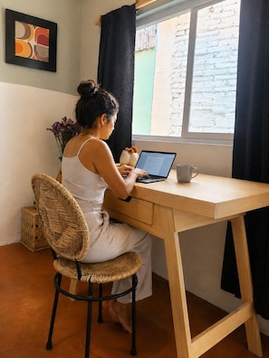 A person seated at a wooden desk with a laptop, a mug, and a vase of flowers. - Our guests appreciate the prime location, comfort, service, and Wi-Fi (Oaxaca de Juárez)
