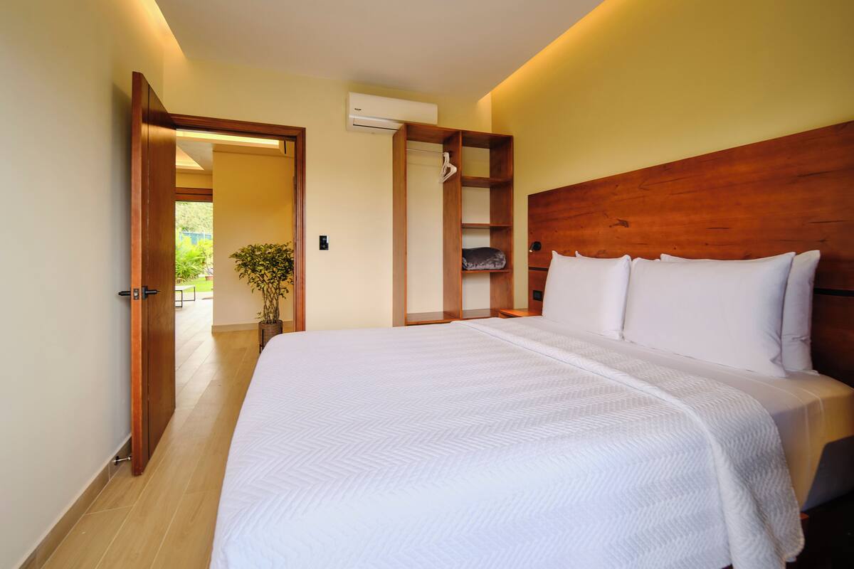 Ein Schlafzimmer mit einem hölzernen Kopfteil, einem großen Bett mit weißer Bettwäsche, einer Klimaanlage und einer Pflanze.