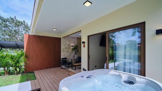 A hot tub on a wooden deck with a stone wall and a door leading to a covered patio. - Arenal Volcanic Villas (La Fortuna)
