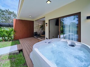 A hot tub on a wooden deck with a stone wall and a door leading to a covered patio. - Arenal Volcanic Villas (La Fortuna)