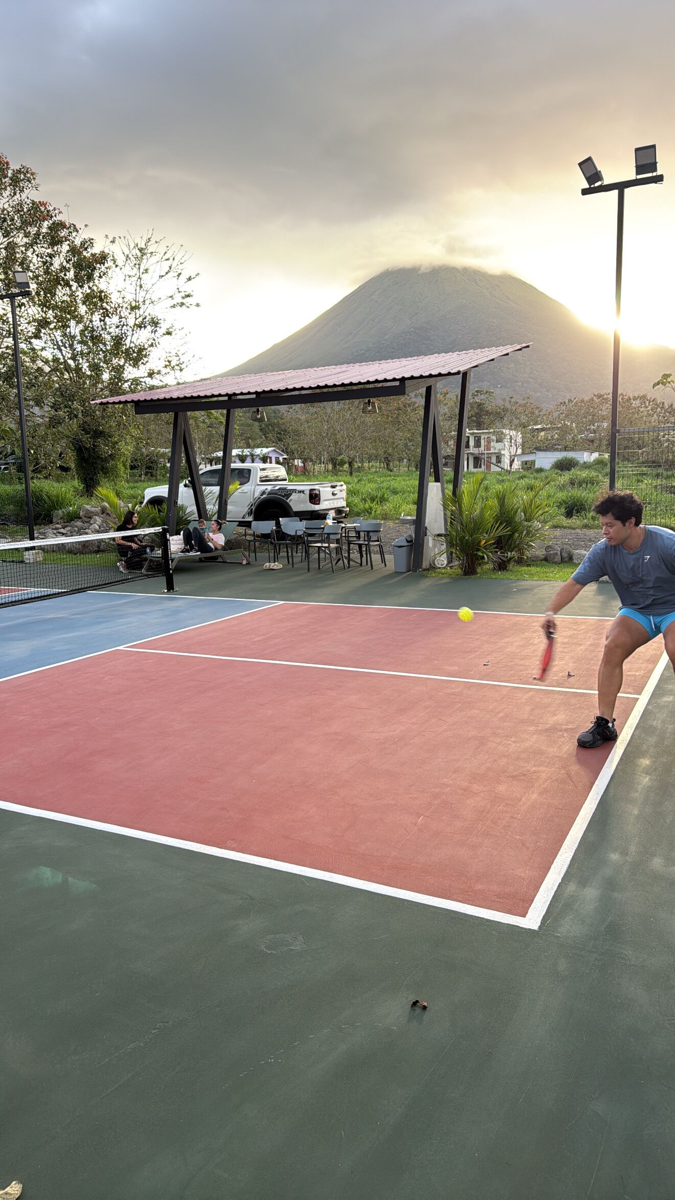 A tennis court with a net, a pavilion, and a mountain in the background.