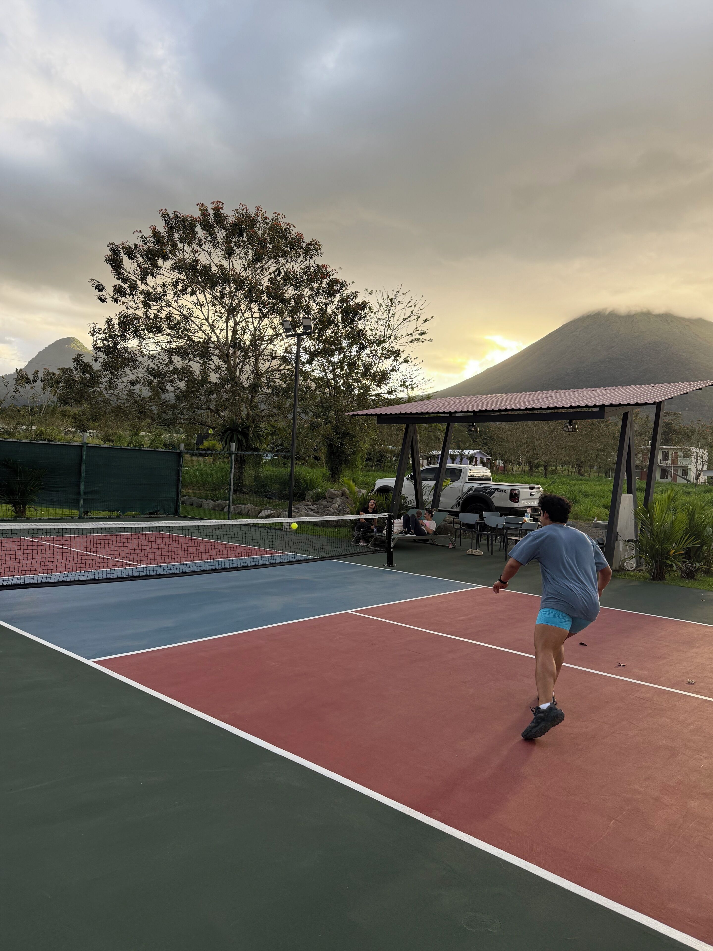 Een tennisbaan met een net, een paviljoen en een berg op de achtergrond.