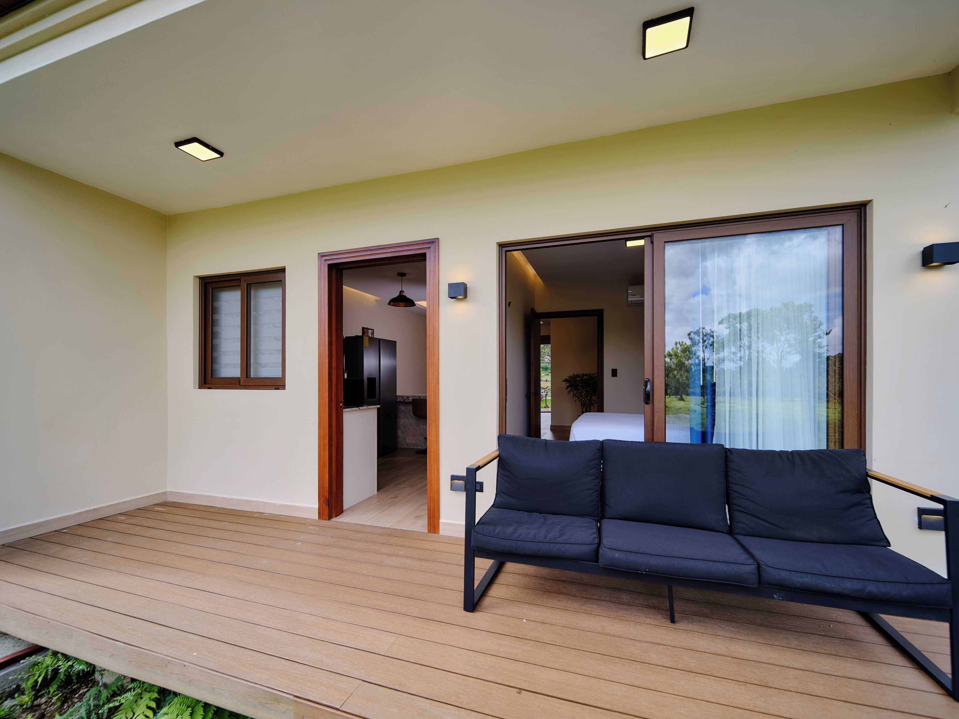 A modern room with a wooden floor, a dark sofa, and a large sliding glass door leading to a bedroom.