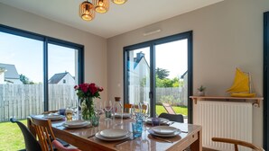 Un comedor con una mesa preparada para cuatro personas, ventanas amplias y vista al jardín trasero.