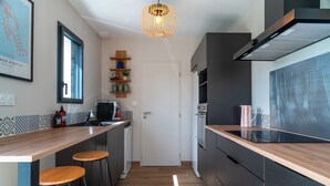 Una cocina moderna con encimera de madera, dos taburetes de bar, horno integrado y una lámpara colgante.
