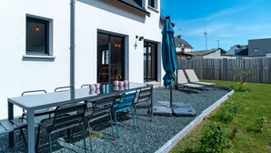 Una casa moderna con un patio, una mesa con sillas y un paraguas azul.