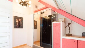 Une salle de bain avec une douche en verre, un plancher en bois, un mur blanc orné d’un tableau encadré et un meuble rouge.