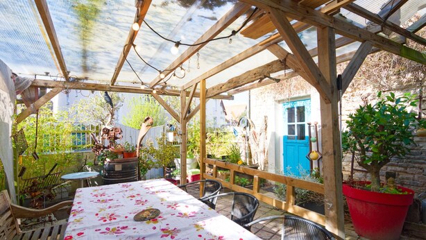 Un espace extérieur abrité, doté d’une table et de chaises, de poutres en bois et de plantes en pot.