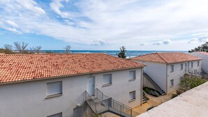 Un quartier résidentiel en bord de mer, avec des bâtiments aux toits de tuiles en terre cuite, un ciel dégagé et une vue sur la mer.