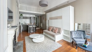 Un soggiorno moderno con un divano, due tavolini rotondi, una poltrona grigia e una cucina sullo sfondo.