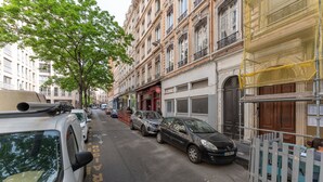 Una strada con auto parcheggiate, edifici con balconi e un albero.