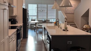A modern kitchen with white cabinets, a central island, pendant lighting, and a dining area with a table and chairs. - FIFA 2026 RETREAT - 2BR Sleeps 6 - Bikes - BeltLine to Stadium - Walkable (Atlanta)