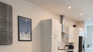 A modern living room with a sofa, a coffee table with a plant, and a kitchen area with white cabinets and appliances. - FIFA 2026 RETREAT - 2BR Sleeps 6 - Bikes - BeltLine to Stadium - Walkable (Atlanta)
