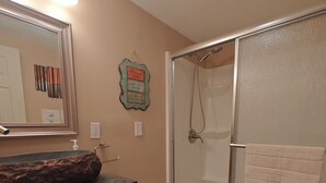 Ein Badezimmer mit einem Holzkosmetikschrank, Toilette, Dusche mit Glastür und einem beleuchteten Spiegel.