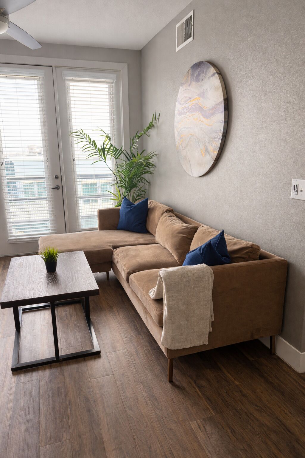 Una sala de estar con un sofá modular, una mesa de centro, una planta en maceta y una obra de arte abstracto colgada en la pared.