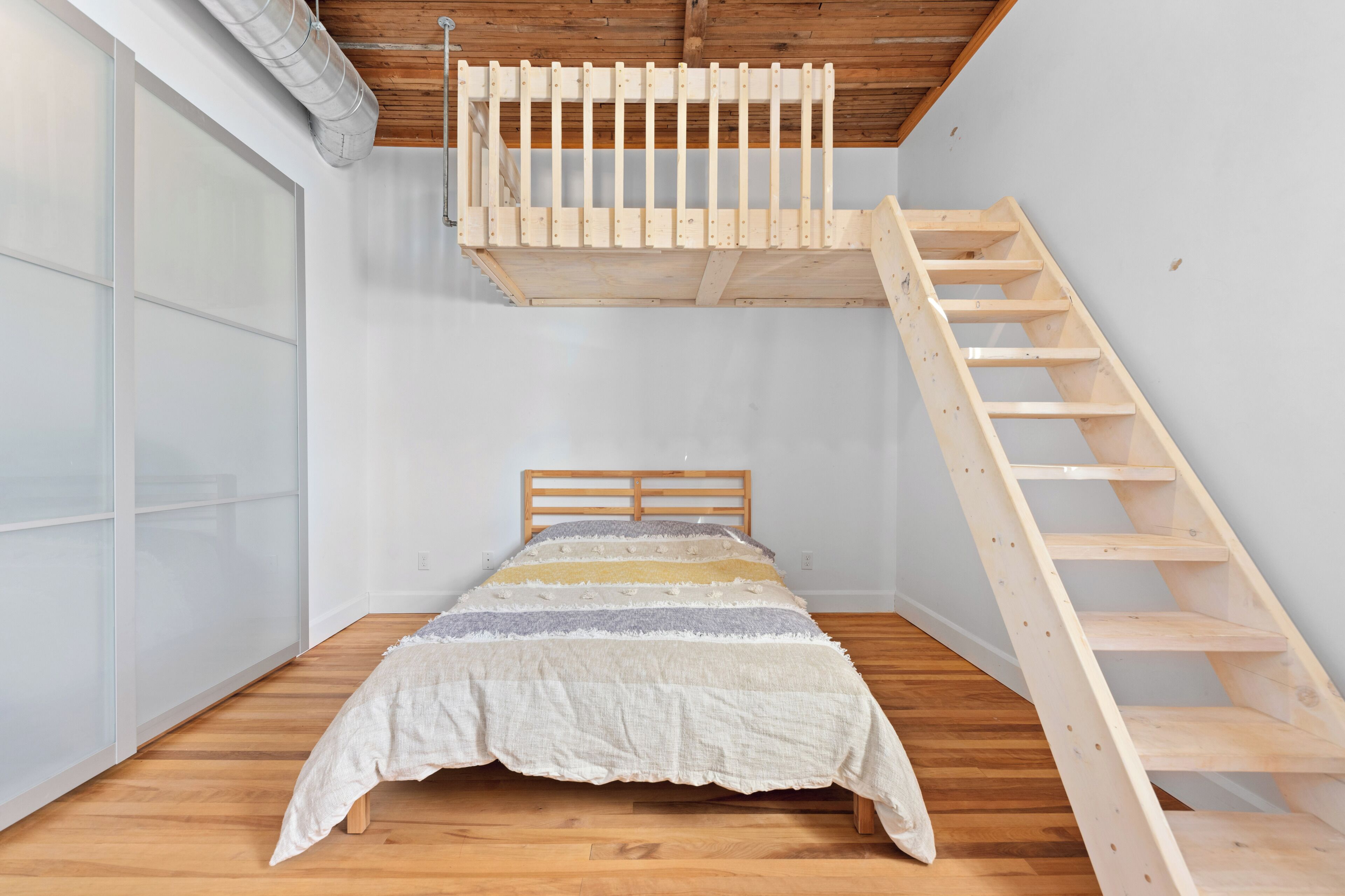Une chambre avec un lit en bois, une échelle en bois et une porte coulissante.