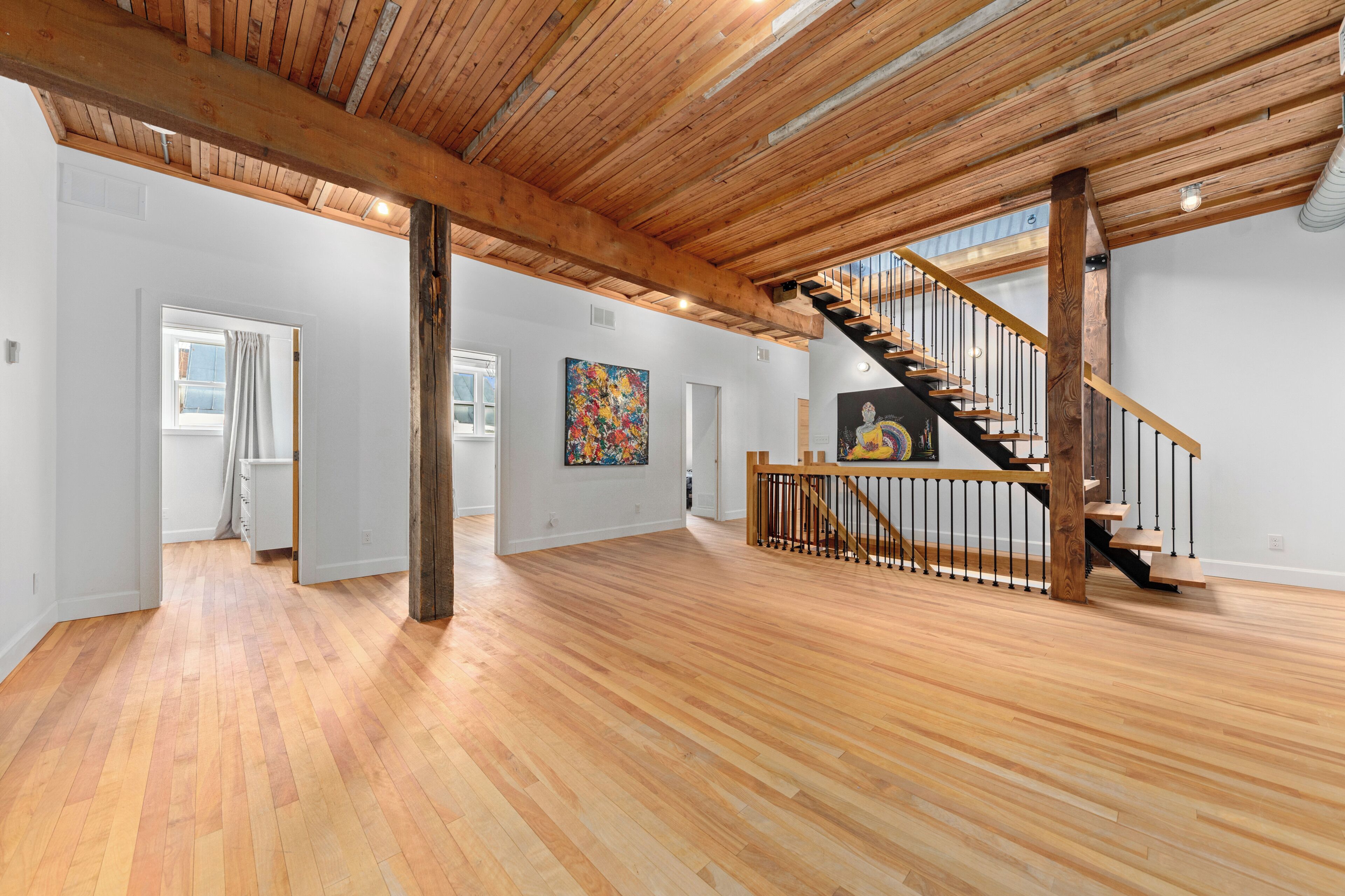 A spacious interior with wooden floors, a staircase with a wooden railing, and a large abstract painting on the wall.