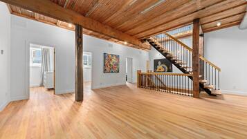 A spacious interior with wooden floors, a staircase with a wooden railing, and a large abstract painting on the wall.