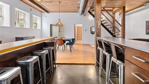 A modern kitchen with a bar area, wooden ceiling, and a staircase leading to an upper level. - Rêve St-Viateur (Joliette)