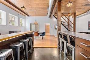 A modern kitchen with a bar area, wooden ceiling, and a staircase leading to an upper level.