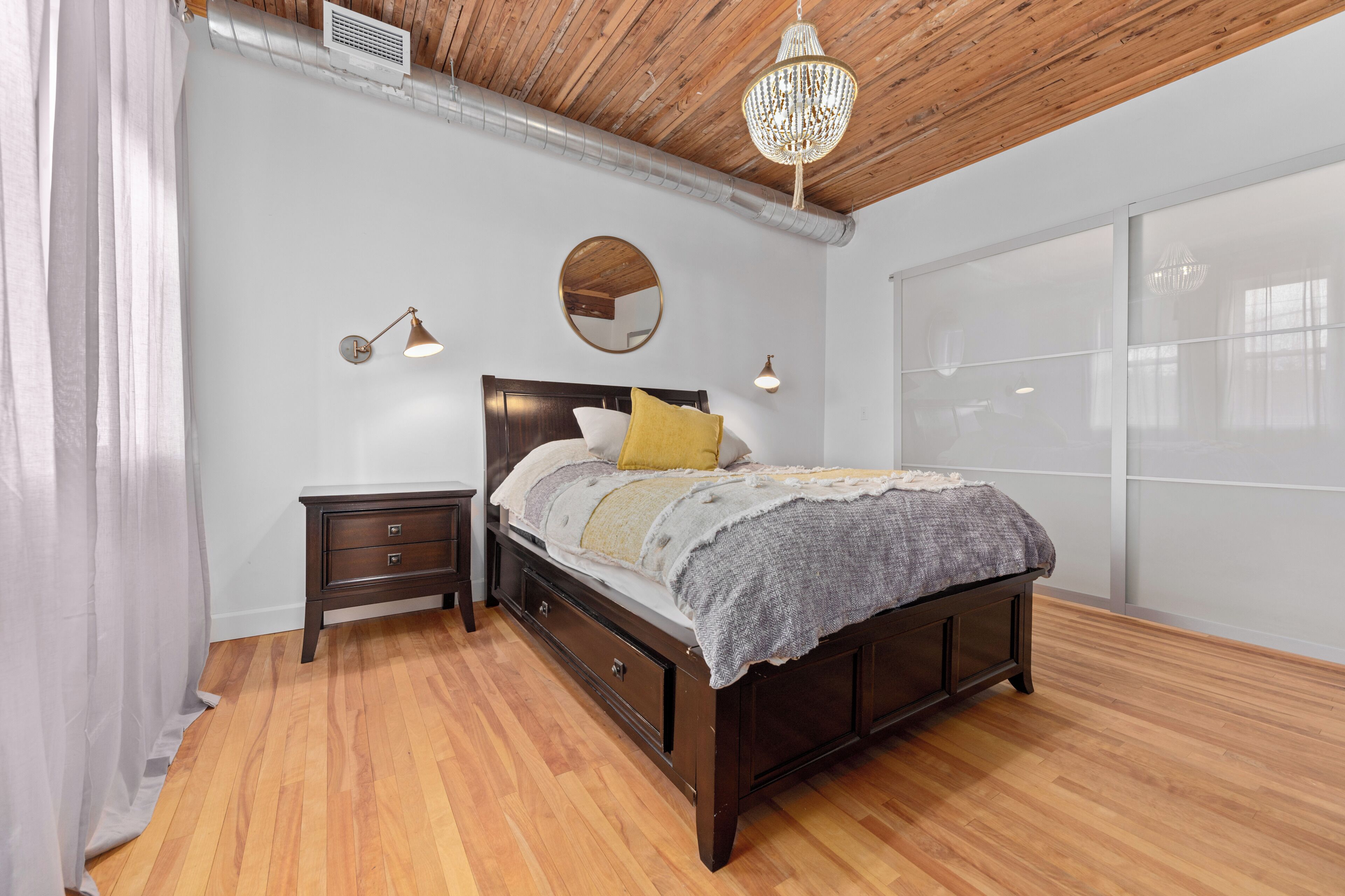 A bedroom with a wooden ceiling, a bed with a headboard, bedside tables, and a large window.