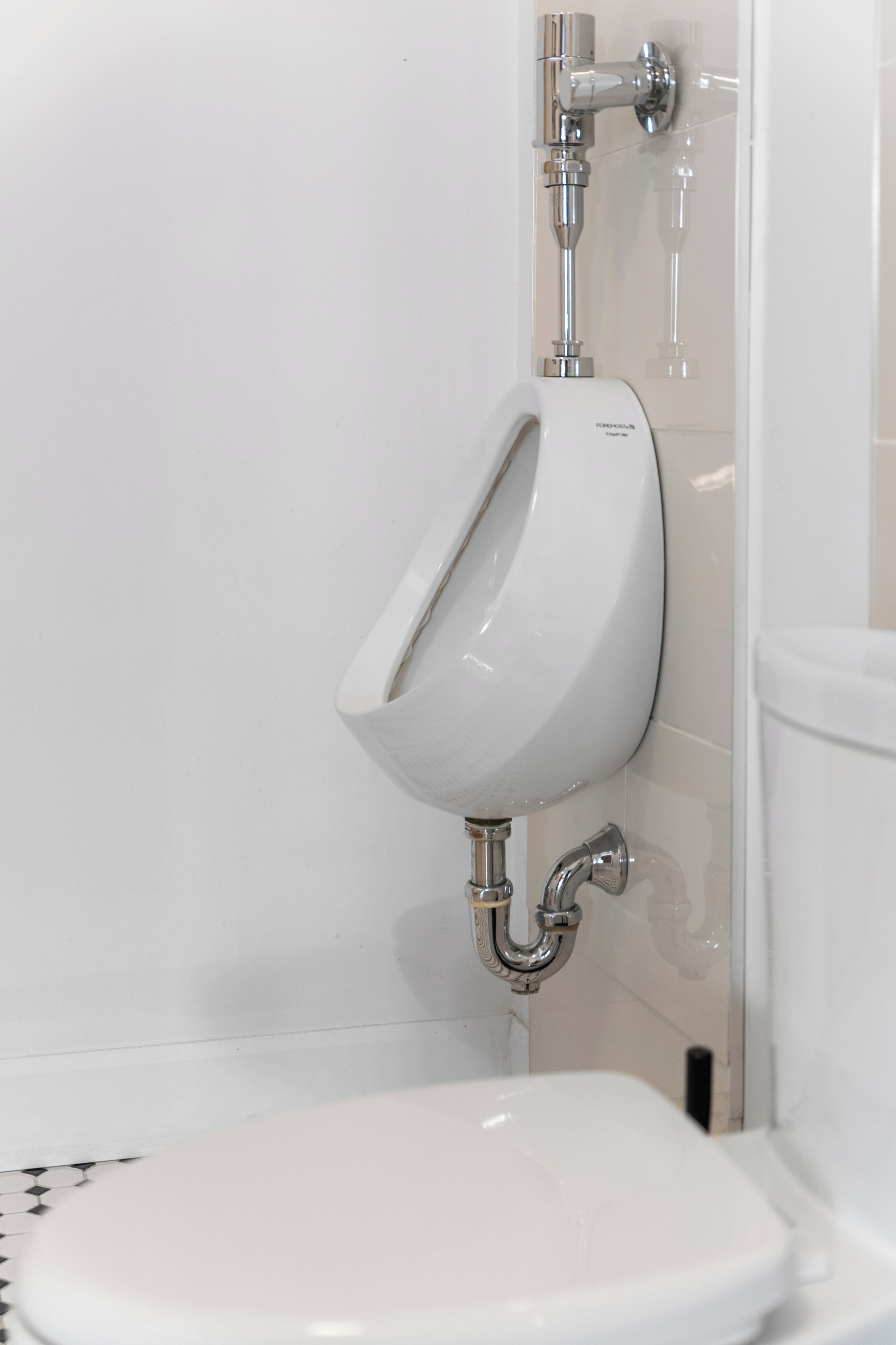 Une salle de bain moderne équipée d’un urinoir, de toilettes et dont la tuyauterie est visible.