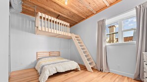 A bedroom with a wooden ladder, a bed, a window with curtains, and a wooden ceiling. - Rêve St-Viateur (Joliette)