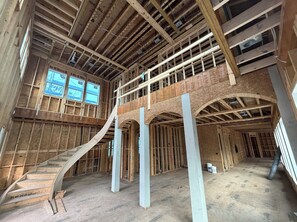 A multi-level building under construction with exposed wooden beams, a staircase, and a large window. - New Construction, Quick Walk to Beach, Chefs Kitchen, Pool, Free Golf (Hilton Head Island)