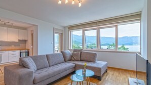 Ett modernt vardagsrum med en soffa, ett soffbord i glas och utsikt över berg genom stora fönster.