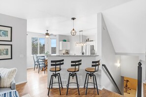 A modern kitchen with a central island, bar stools, pendant lighting, and a staircase leading to an upper level. - Hot Tub + Gym + Workstations | Family Favorite (Broomfield)