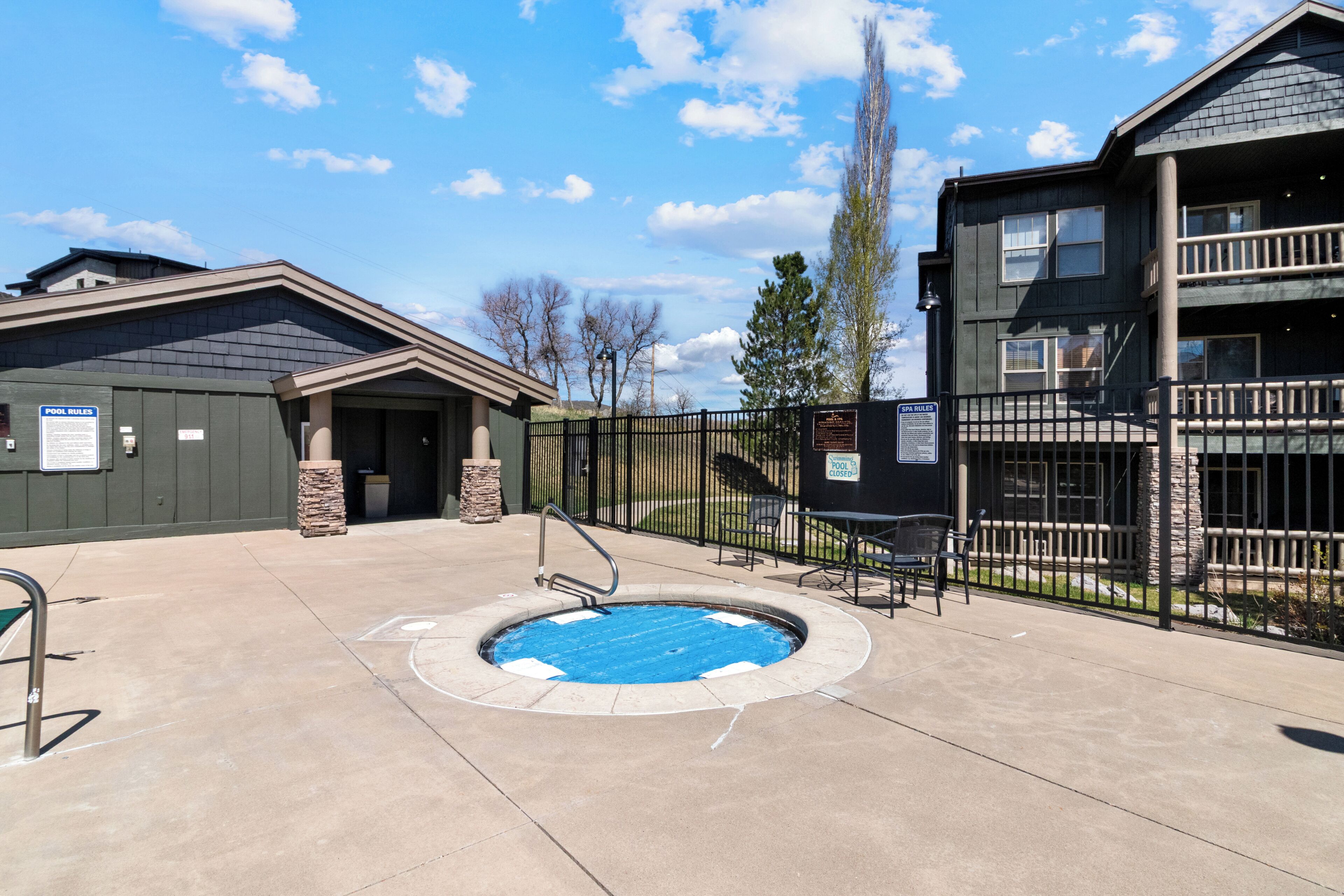 A pool area with a hot tub, a covered seating area, and a building with a balcony.