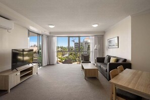 A modern living room with a flat-screen TV, a sofa, a coffee table, and a dining table. - Coastal Escape - Sun City (Gold Coast)