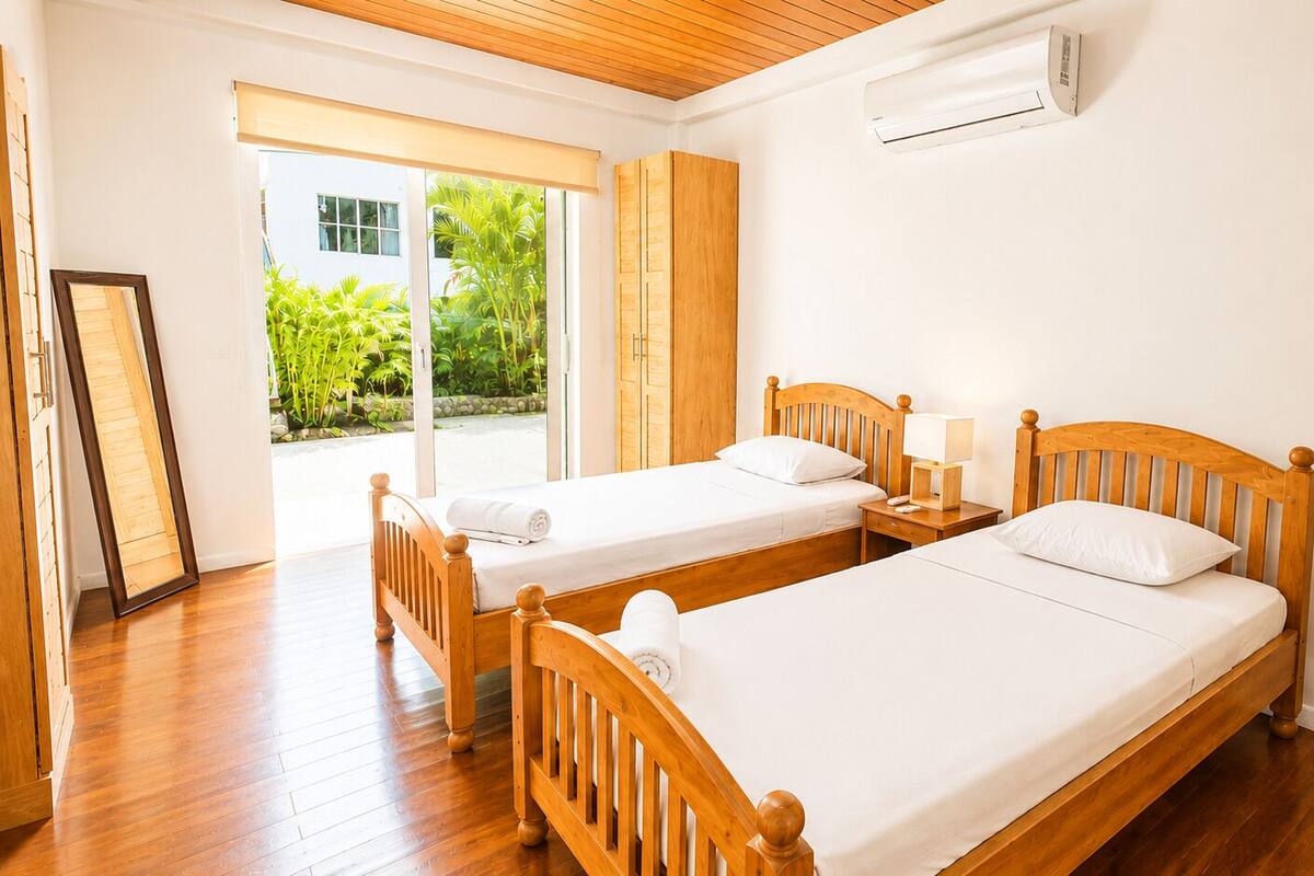 Une chambre avec deux lits en bois, une fenêtre donnant sur un paysage verdoyant et un appareil de climatisation.