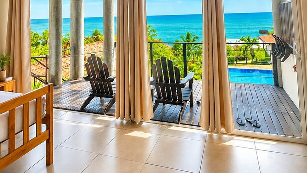A room with a wooden ceiling, large windows, a view of the ocean, a pool, and two Adirondack chairs. - LAOLA SURF RESIDENCE (El Sunzal)