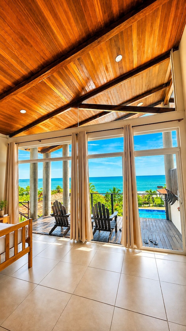 A room with a wooden ceiling, large windows, a view of the ocean, a pool, and two Adirondack chairs. - (El Sunzal)