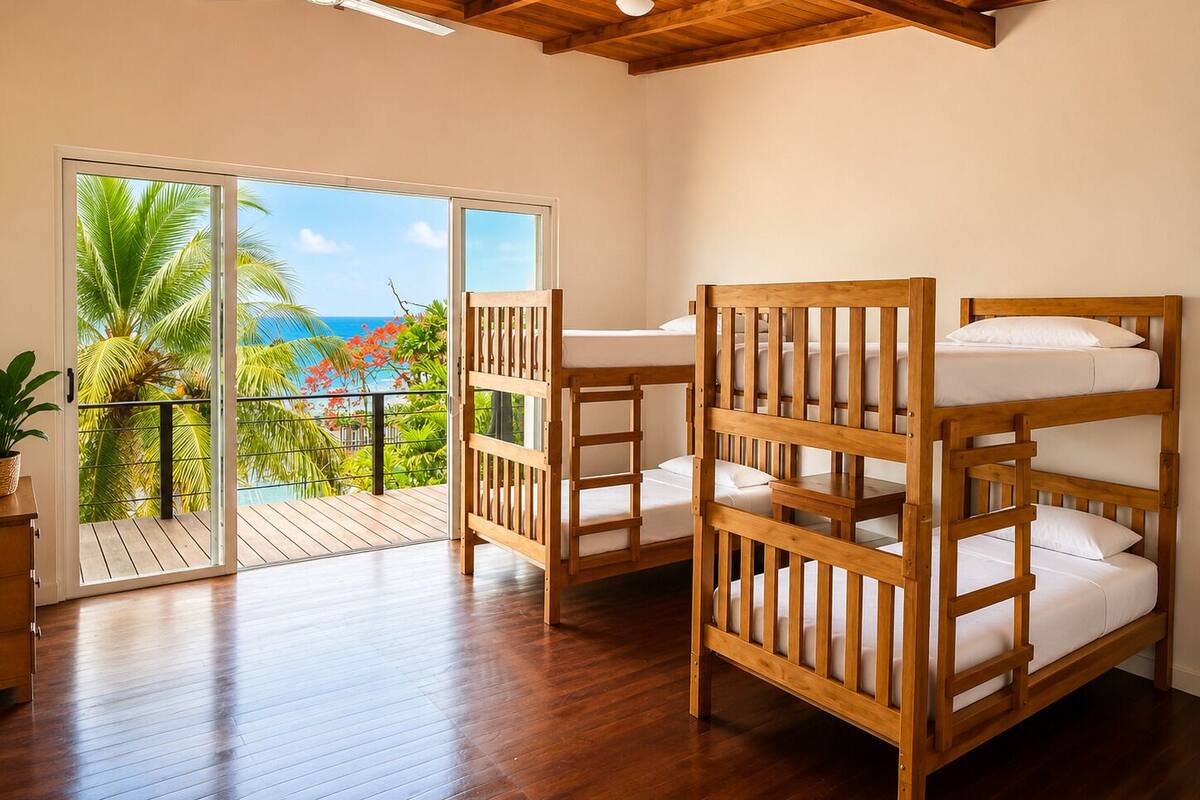 Une chambre avec des lits superposés en bois, un bureau en bois et un balcon donnant sur l’océan.