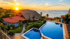 A resort with a wooden deck, two swimming pools, and a view of the ocean at sunset. - LAOLA SURF RESIDENCE (El Sunzal)